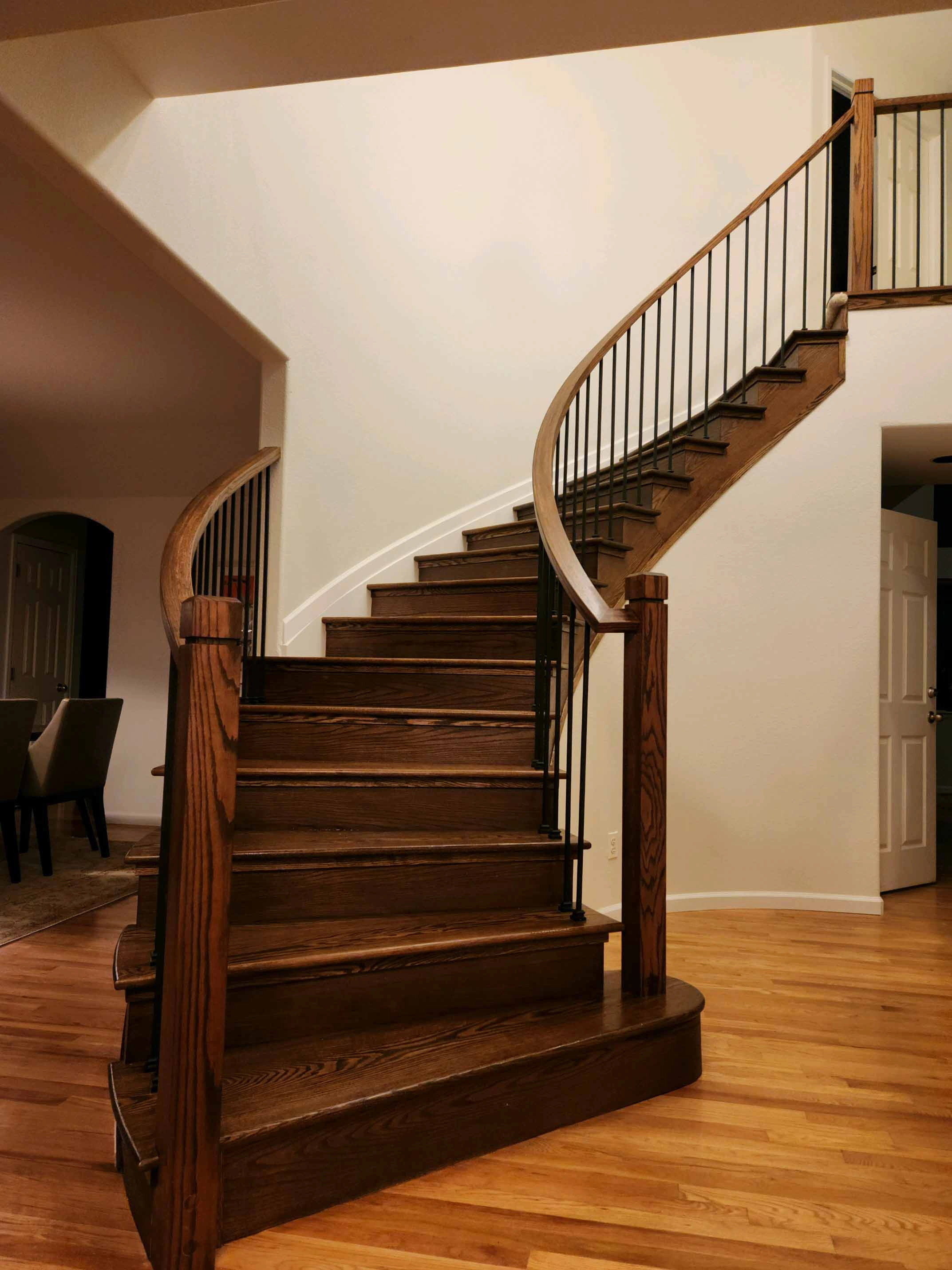 Curved stair railing with stained handrail and iron balusters